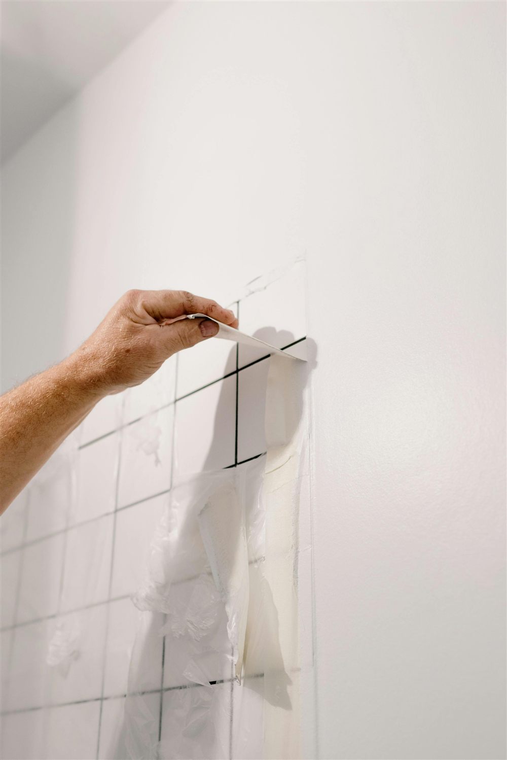 Main retirant une protection de joint sur un carrelage mural